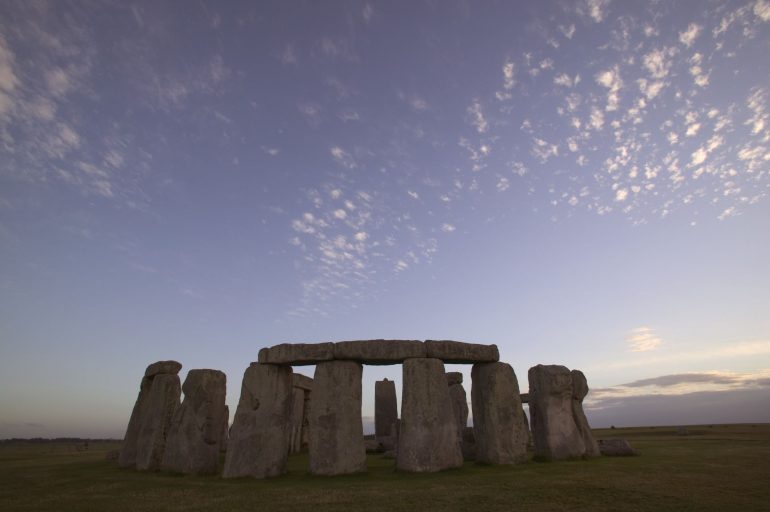 The great and ancient stone circle of Stonehenge, one of the wonders of the world. Stonehenge, Wiltshire, England. Prehistoric henge. Dusk, sunset, sunrise,wispy cloud. Low angle surface view.