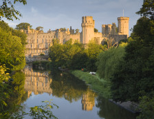 Warwick Castle and the River Avon, Warwick, Warwickshire, UK. View of Warwick Castle from the River Avon. Grand castle. Trees and green space next to the river.