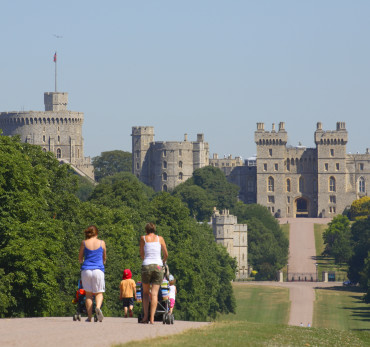 Two mothers with their young children, pushing prams along the Long Walk towards Windsor Castle in the distance. The Long Walk was commenced by Charles II from 1680-1685 by planting a double avenue of elm trees. The central carriage road was added by Queen Anne in 1710. It is a little less than three miles long. To the south of Windsor is The Great Park extending over some 14,000 acres of which 8,000 acres are forest. The public areas are predominantly woodland or open grassland.