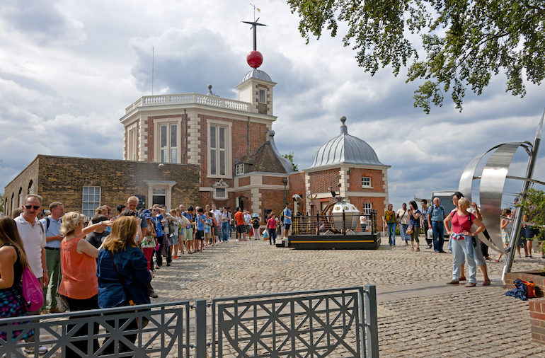 Visitors queuing to take pictures on the line of the Prime Meridian at the Royal Observatory, Greenwich, London. Photo Credit: © Daniel Case via Wikimedia Commons.